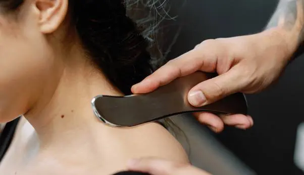 Therapist scraping neck with tool.